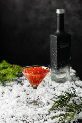 Wall Mural - Red salmon caviar in a martini glass on and a bottle of vodka in the snow. Copy spase