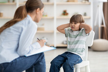 Professional Psychotherapist Trying To Talk To Difficult Kid, Grumpy Little Boy Covering Ears And Frowning Nose
