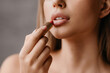 © Prostock-studio - Lip skincare and beauty treatments concept. Young woman with perfect skin applying nude lipstick, doing morning routine
