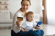 Happy young mother and her son using smartphone and doing online shopping, woman holding credit card in hand
