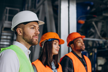 Three factory workers in safety hats discussing manufacture plan