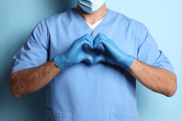 Poster - Doctor making heart with hands on light blue background, closeup