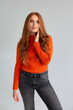 Pretty woman with long red hair in orange jumper isolated on light grey