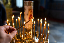 Candles In Russian Orthodox Cathedral With Icons On Background. Hand Putting Candle.