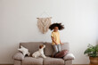 © Evrymmnt - Little black girl playing with her friend, the adorable wire haired Jack Russel terrier puppy at home. Preschooler jumping on the couch with rough coated pup. Interior background, close up, copy space