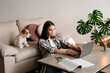 Portrait of young beautiful hipster woman working on a laptop with her adorable wire haired Jack Russel terrier puppy at home. Female with rough coated pup. Interior background, close up, copy space.