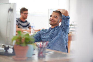 Leinwandbilder - He knows he has the answer. Young creative professional smiling at his pc in a bright communal office space.