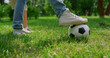 Unknown human legs kicking ball on grass closeup. Father play football with son.