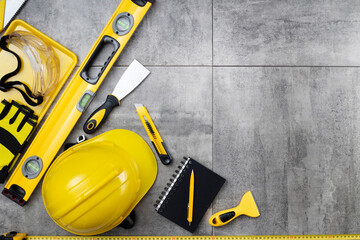 Sticker - Contractor theme. Tool kit of the contractor: yellow hardhat, libella, hand saw. Plans and notebook on the gray tiles.