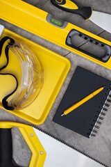 Sticker - Contractor theme. Tool kit of the contractor: yellow hardhat, libella, hand saw. Plans and notebook on the gray tiles.