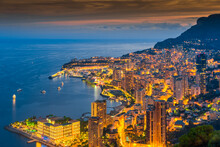 Aerial view of Monaco - Monte-Carlo at dusk, cityscape with night illumination, mountain, skyscrapers, mediterranean sea