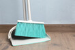 Plastic broom with dustpan near light blue wall indoors