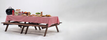 Picnic Table And Red Checkered Tablecloth With Food And Drink For Outdoor Party. Isolated White Background. Wooden Party Table With Foods And BBQ Grills Stove For Summer Picnics Activities. Isolate.