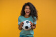 © wpadington - Studio image of excited soccer fan girl holding ball in hands looking at the camera with amazed face expression, celebrating her favorite team victory
