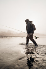 Fly Fisherman Wading In The River On A Foggy And Cold Morning During Sunrise