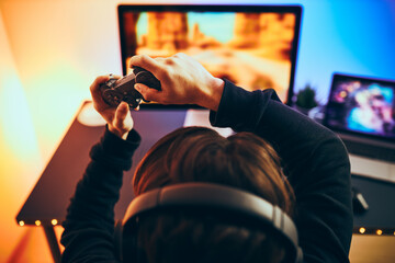 Wall Mural - Man playing video game at home. Gamer holding gamepads sitting at front of screen. Streamer playing online in dark room lit by neon lights. Competition and having fun