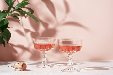 Two crystal glasses of rose sparkling wine or champagne on pastel pink marble table in sunlight. Minimal creative composition with copy space. Summer drink concept.