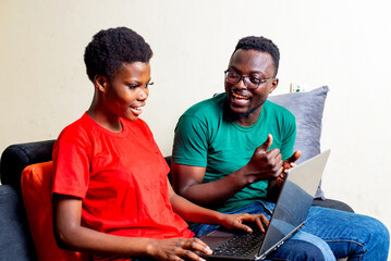 Sticker - young couple sitting on a sofa at home using a laptop while smiling.