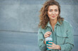 © Evgeniya Grande - Close-up urban portrait of smiling beautiful and confident woman 25-30 years old with curly hair, mint blue clothes and perfect skin, holding in hands takeaway cold soda drink. Copy space
