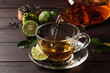 Pouring bergamot tea into glass cup at wooden table, closeup