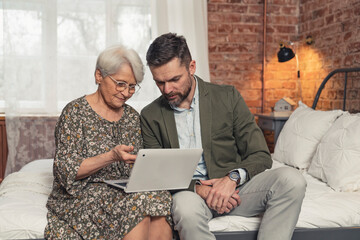 modern retired mother in her 70s showing her middle-aged son something on her laptop. High quality photo