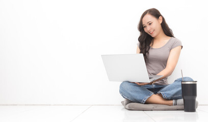 Wall Mural - Beautiful Asian woman wearing grey casual shirt using laptop on white background and copy space.  Cute Asian woman sitting on the floor room relaxing for work from home concept