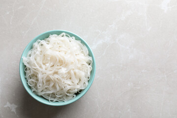 Wall Mural - Bowl of tasty cooked rice noodles on light grey table, top view. Space for text