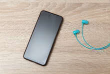 Smartphone With Blue Wired Earphones On Wooden Table