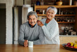 Portrait of happily retired elderly biracial couple standing, smiling at camera in their modern kitchen.