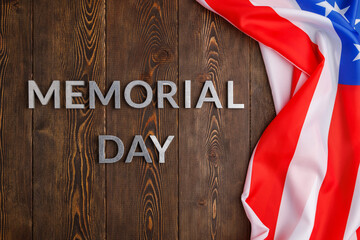 the words memorial day laid with silver metal letters on wooden board surface with crumpled usa flag