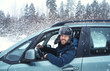 © Gargonia - Happy positive man driver looking on camera thowth window of his car enjoying snowy day on country road.  Road trip, winter vacation. Driving auto in cold season.