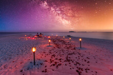 Amazing Beach Dinner Setting Under Milky Ways Night Sky. Luxury Destination Dining, Honeymoon Or Anniversary Dinner, Flowers And Candles For The Best Romantic Experience. Stunning Colorful Outdoors