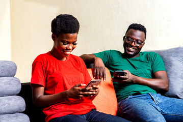 Poster - young happy couple each using mobile phone at home.