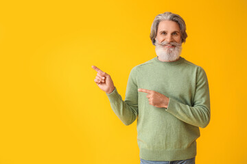 Sticker - Handsome senior man in knitted sweater pointing at something on yellow background