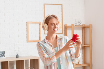 Young woman with wireless portable speaker and headphones in light room