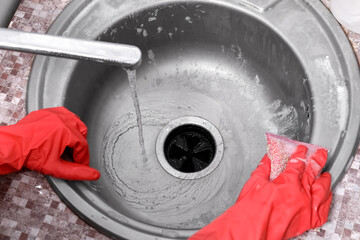 Housewife in rubber gloves cleaning silver sink with sponge, closeup