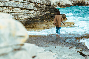 Wall Mural - woman walking by rocky sea beach at sunny windy day. summer vacation