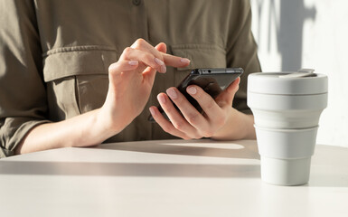 Poster - Woman hands closeup holding phone. Woman sitting at table and typing message, surfing Internet or using phone applications for orderings, shopping, bank transactions. High quality photo