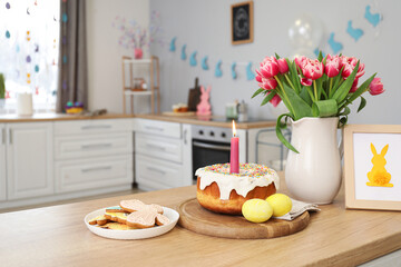 Easter cake, candle, eggs, cookies, picture and vase with tulips on counter in kitchen