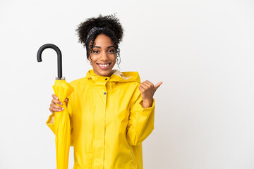 Wall Mural - Young woman with rainproof coat and umbrella isolated on white background pointing to the side to present a product