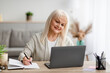 © Prostock-studio - Mature woman writing and using laptop at home