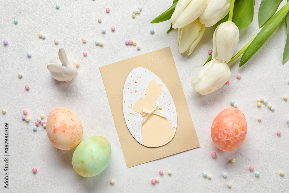 Beautiful Easter composition with greeting card, painted eggs, bunny and flowers on light background