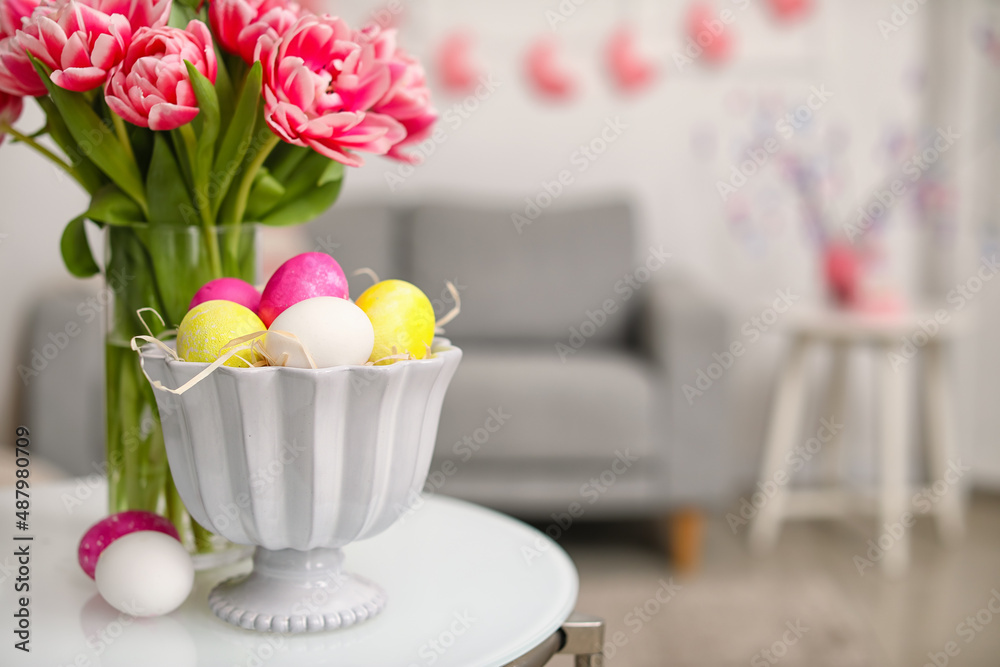 Vase with tulips and Easter eggs on table in room, closeup