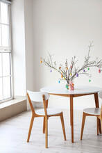 Tree Branches Decorated With Easter Eggs In Vase And Rabbit On Dining Table In Light Room