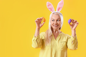 Poster - Mature woman with bunny ears and Easter eggs on yellow background