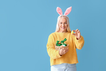 Wall Mural - Mature woman with bunny ears and Easter basket on blue background