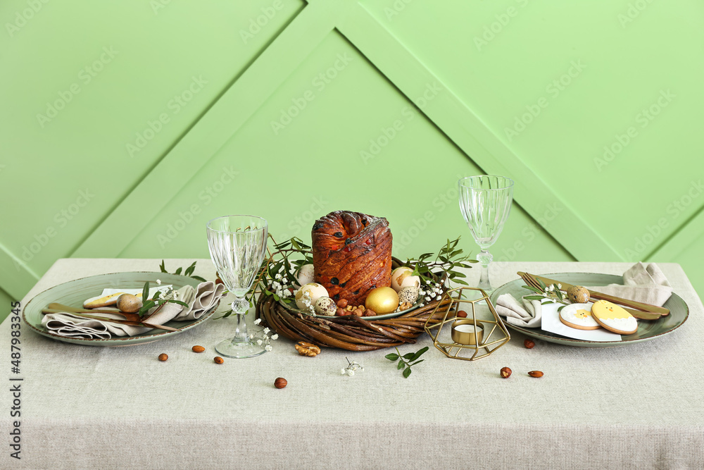 Dining table with beautiful setting for Easter celebration with cookies near green wall