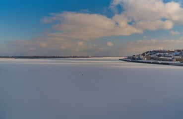 Panorama of the confluence of two large rivers. The snow-covered expanse of the mouth of a frozen river. Landscape of urban expanses with ancient city buildings. A fisherman on a winter fishing trip w