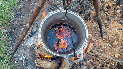 Wall Mural - Mulled wine in a tourist pot over hot camp fire. Mulled wine by the fire. Mulled wine cooked on fire outdoors. Picnic.