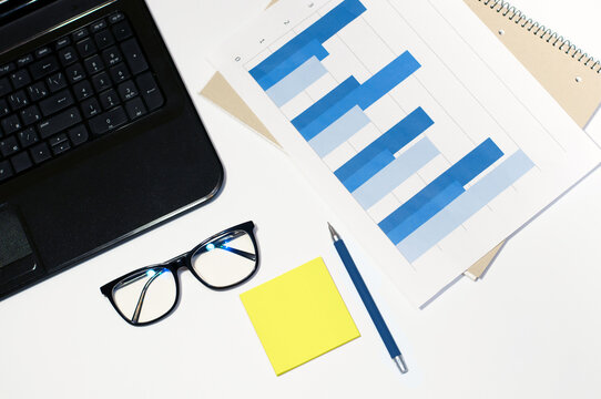 on the bright desktop there are glasses, calculator, laptop, pen and graphics. High quality photo
